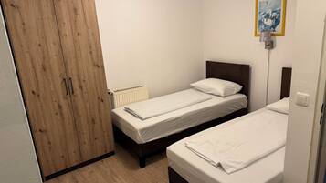 Ein kleines, sauberes Zimmer mit zwei Einzelbetten, einem Holzschrank und einer Heizung.
