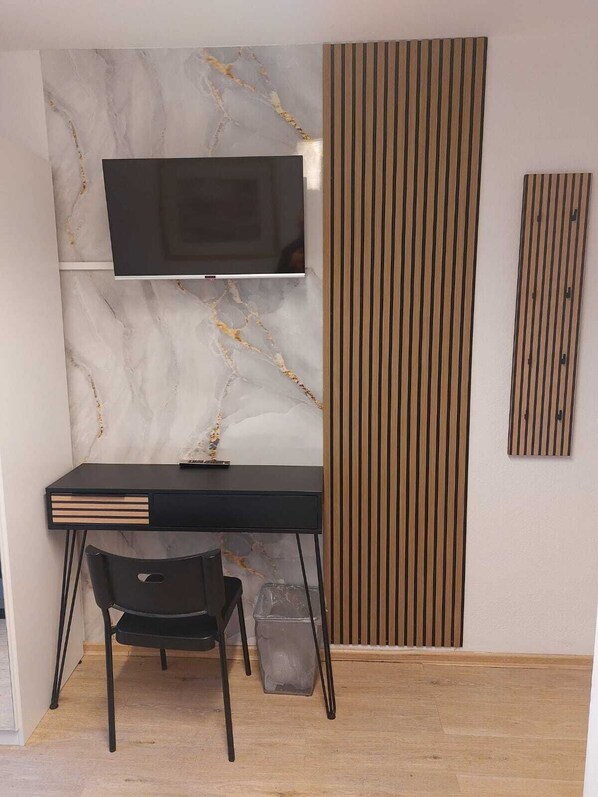 A modern workspace with a marble wall, a mounted TV, a black desk, and a chair. - Pension Alpha (Frankfurt)