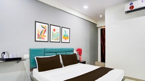A hotel room with a bed, a nightstand, a wall-mounted air conditioner, and three framed artworks. - Super Hotel O Dindoli Surat (Surat)
