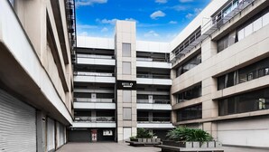 A modern hotel with a central tower, multiple balconies, and a courtyard with planters. - Super Hotel O Dindoli Surat (Surat)
