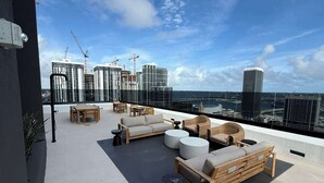 A rooftop terrace with outdoor seating, a view of the city skyline, and construction cranes in the background. - Downtown Miami 1BR Walk to Bayside Kaseya Gym Pool (Miami)