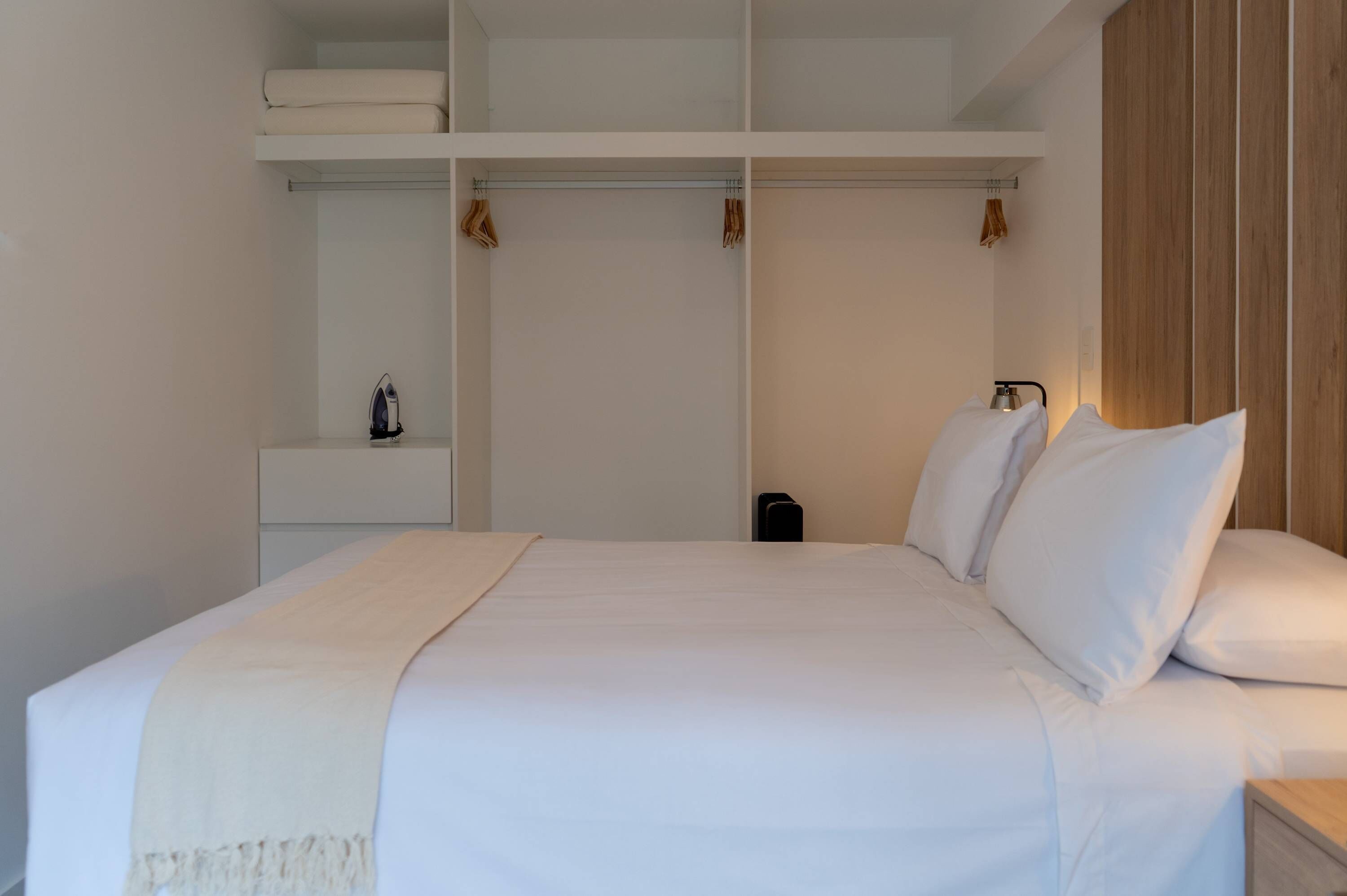 Une chambre bien rangée, avec un lit, une armoire et une étagère sur laquelle se trouve une lampe.