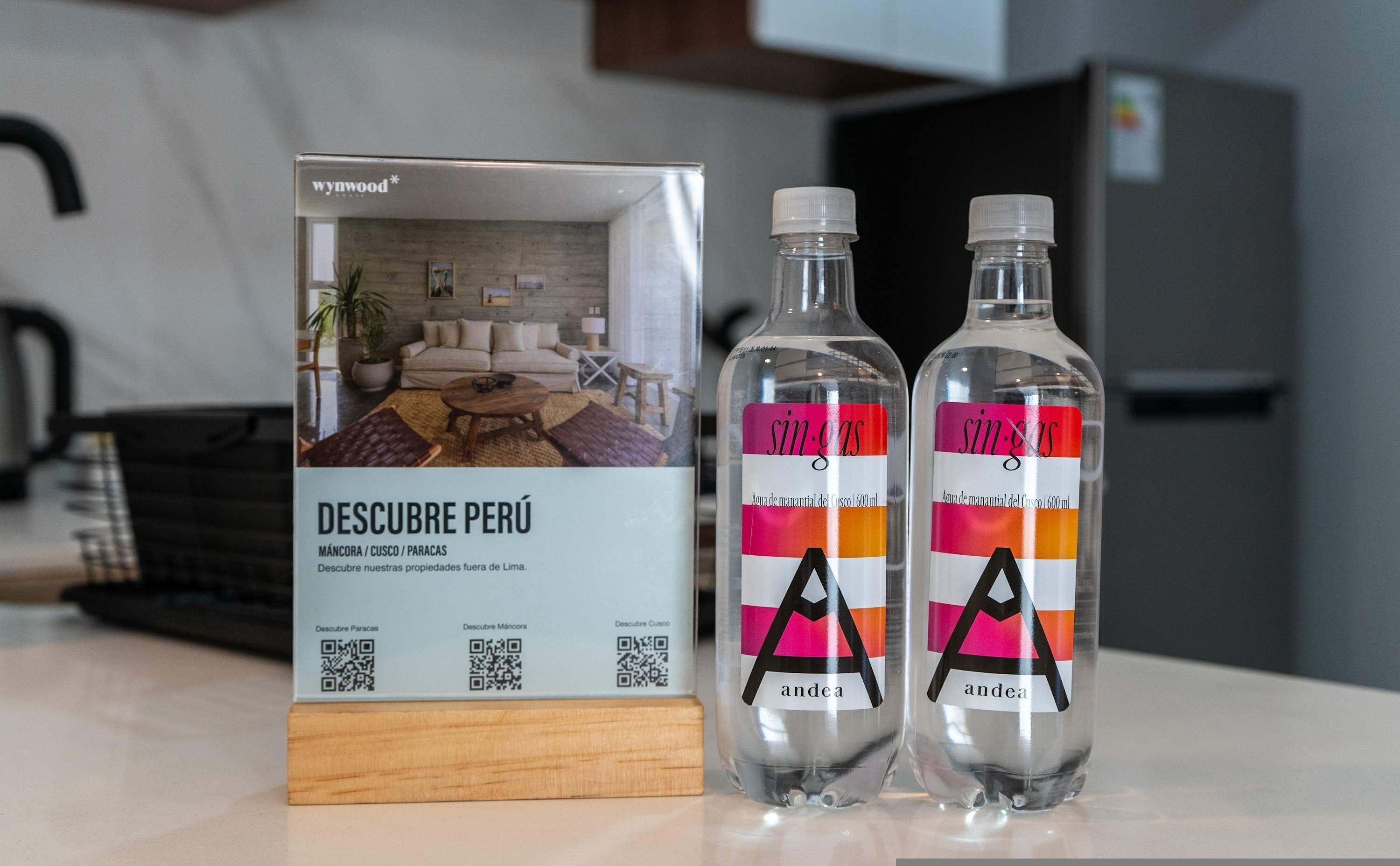 Eine Broschüre und zwei mit 'sin-gas' beschriftete Wasserflaschen, jeweils mit QR-Code, sowie ein Holzklotz.