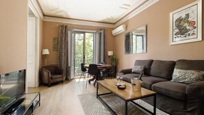 Een moderne woonkamer met een flatscreen televisie, een bruine leren bank, een houten salontafel, en een eethoek met een tafel en stoelen.