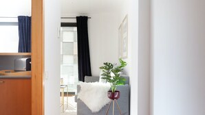 A modern living room with a grey sofa, a white furry throw, and a potted plant on a tripod stand. - Enjoy Apartments Maria (Barcelona)