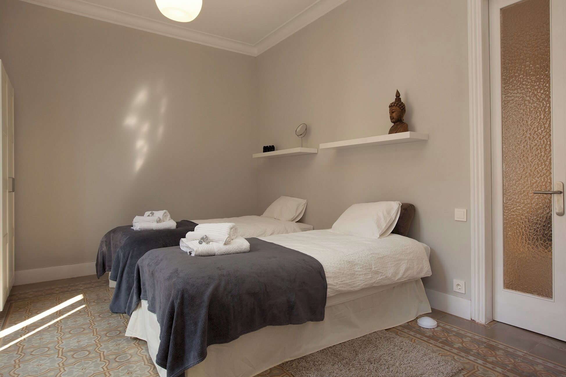 Ein Schlafzimmer mit zwei Betten, einer kleinen Ablagefläche mit Gegenständen und einer Tür mit strukturierter Tapete.