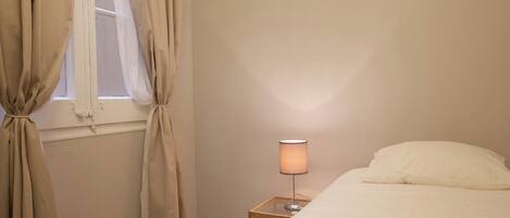 Un dormitorio con una cama, una lámpara de noche y cortinas color beige.