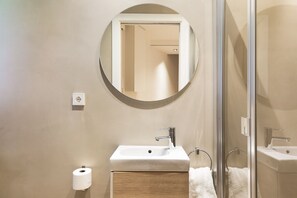 A modern bathroom with a round mirror, a sink, and a glass shower enclosure. - Enjoy Apartments La Riera One (Barcelona)