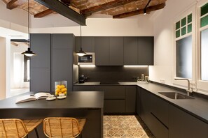 A modern kitchen with dark cabinetry, a central island, a microwave, and a sink. - Enjoy Apartments La Riera One (Barcelona)