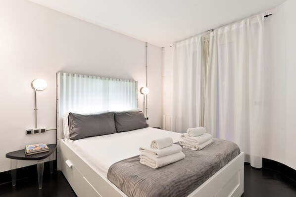 A modern hotel room with a neatly made bed, a small side table with a book, and a bedside lamp. - Eulalias Lodges Barcelona (Barcelona)
