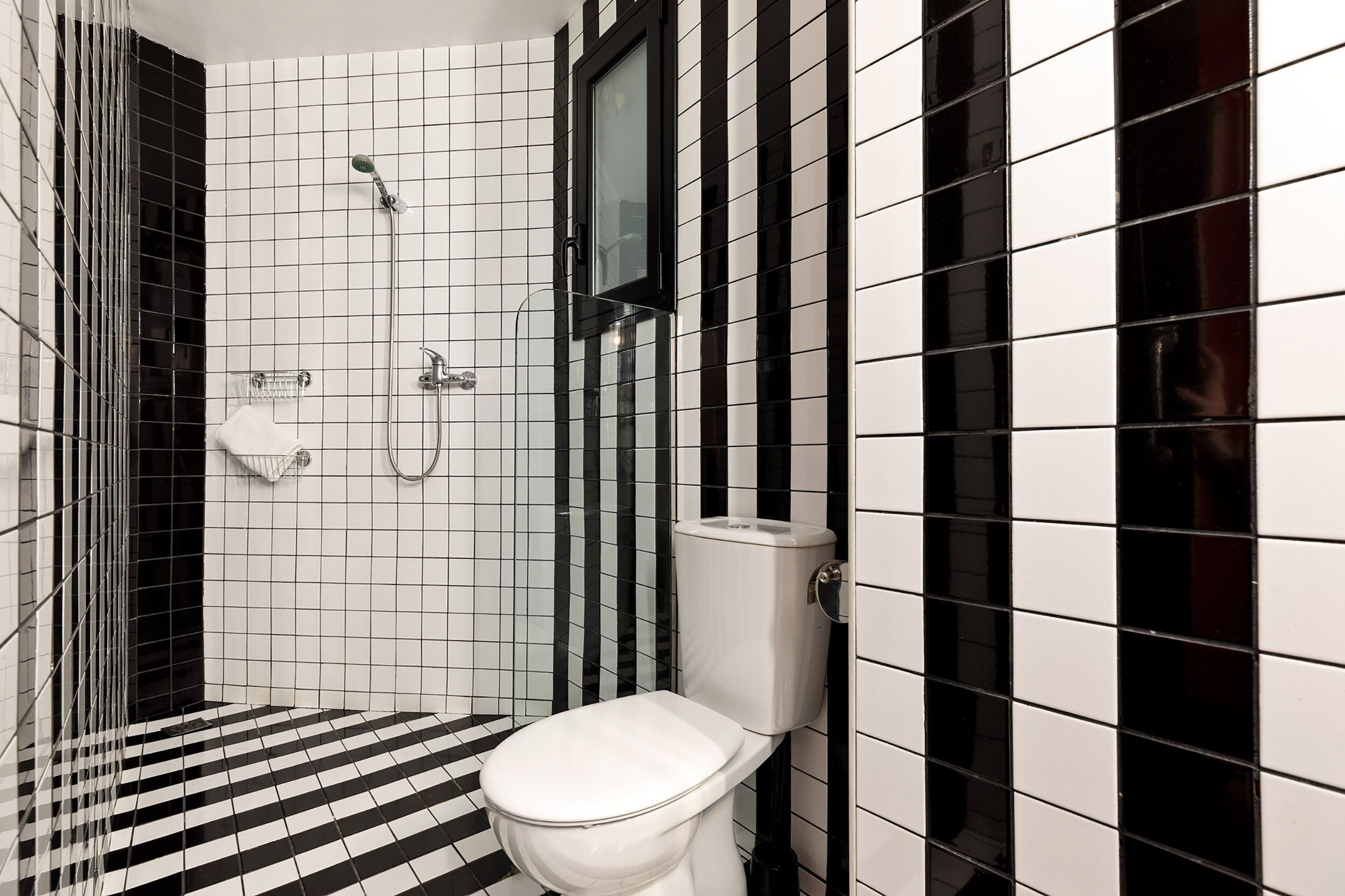 A bathroom with a black and white checkered floor, a white toilet, and a shower area with a glass enclosure.