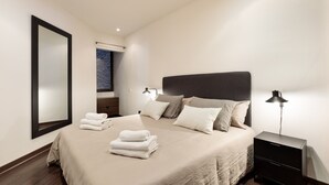 A modern bedroom with a large bed, a nightstand, a mirror, and a window with a view. - Enjoy Apartments Urban Retreat Valencia (Barcelona)