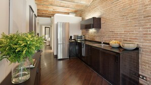 A modern kitchen with a brick wall, stainless steel appliances, and a wooden floor. - Enjoy Apartments Urban Retreat Valencia (Barcelona)