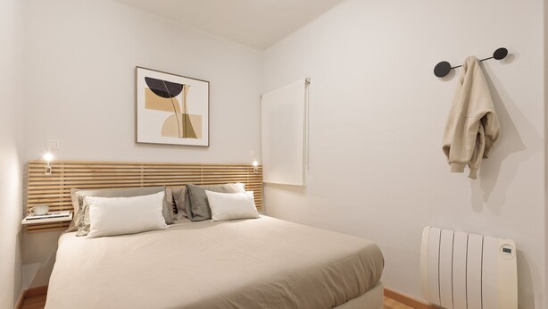 A bedroom with a bed, bedside tables, a wall-mounted radiator, and a towel rack. - Enjoy Apartments Ecuador (Barcelona)