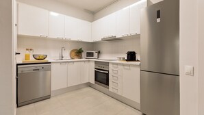 A modern kitchen with white cabinets, stainless steel appliances, and a tiled floor. - Enjoy Apartments Ecuador (Barcelona)