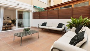 A patio with a sofa, a small table, and chairs. There is a wooden fence and a building in the background. - Enjoy Apartments Ecuador (Barcelona)
