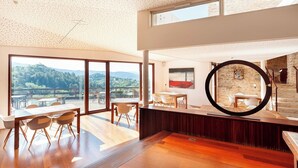 A modern interior with a large dining area, a view of the outdoors, and a stone wall with a circular mirror. - Casa Fumanal - Unique Property for up to 24 (Abizanda)