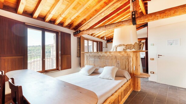 A bedroom with a wooden headboard, a bed with pillows, a wooden table, and a large window. - Casa Fumanal - Unique Property for up to 24 (Abizanda)