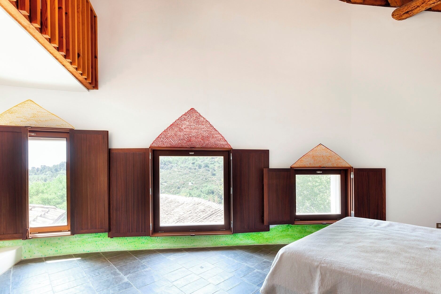 Ein Zimmer mit einem Bett, einem Fenster mit Blick auf Grünflächen und einer Holztreppe.