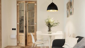 Un salon moderne avec une porte en bois, des chaises blanches, une table ronde et un canapé noir.