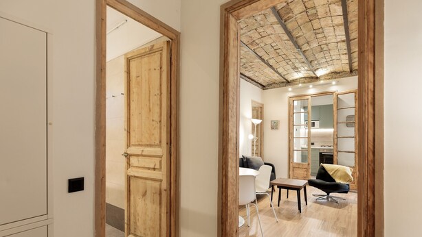 Un couloir avec des portes en bois, un coin repas avec une table et des chaises, et une cuisine équipée de placards et d’une cuisinière.