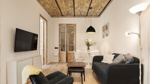 Un salon moderne avec un téléviseur à écran plat, un canapé foncé, une petite table en bois et une chaise blanche.