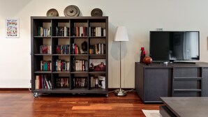 A living room with a bookshelf, a floor lamp, a TV, and a cabinet. - Frida by EnjoyApartments (Barcelona)