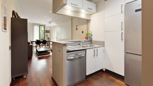 A modern kitchen with a dishwasher, a refrigerator, and a dining area with a table and chairs. - Frida by EnjoyApartments (Barcelona)
