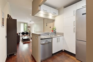 A modern kitchen with a dishwasher, a refrigerator, and a dining area with a table and chairs. - Frida by EnjoyApartments (Barcelona)
