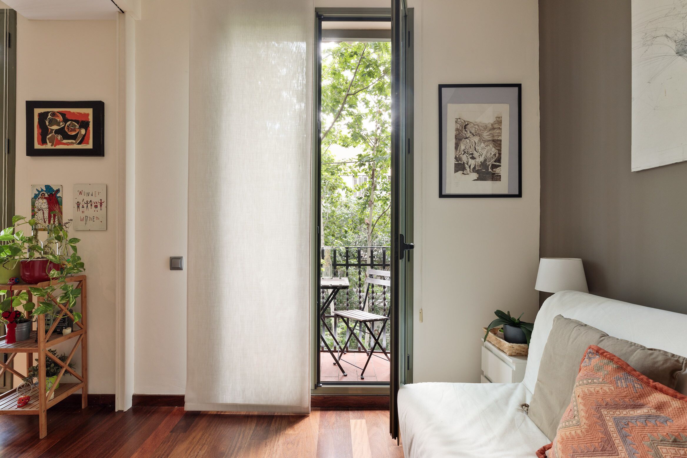 Una stanza con un letto, un comodino, una pianta in vaso e un balcone con tavolo e sedie.