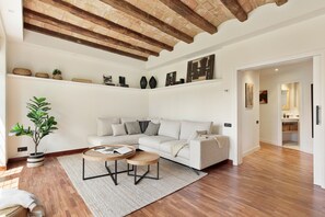 A living room with a white sofa, two wooden side tables, a potted plant, and a brick ceiling. - Enjoy Apartments La Riera Principal (Barcelona)