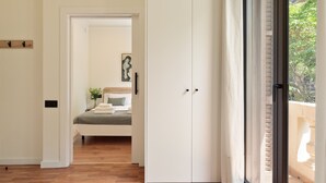 Una camera d'albergo con pavimento in legno, un letto con copriletto grigio, una parete bianca con un quadro e una porta scorrevole che dà su un balcone.