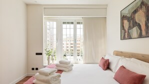 Una camera d'hotel con un letto grande, una finestra con tende, un quadro appeso al muro e vista sugli edifici.