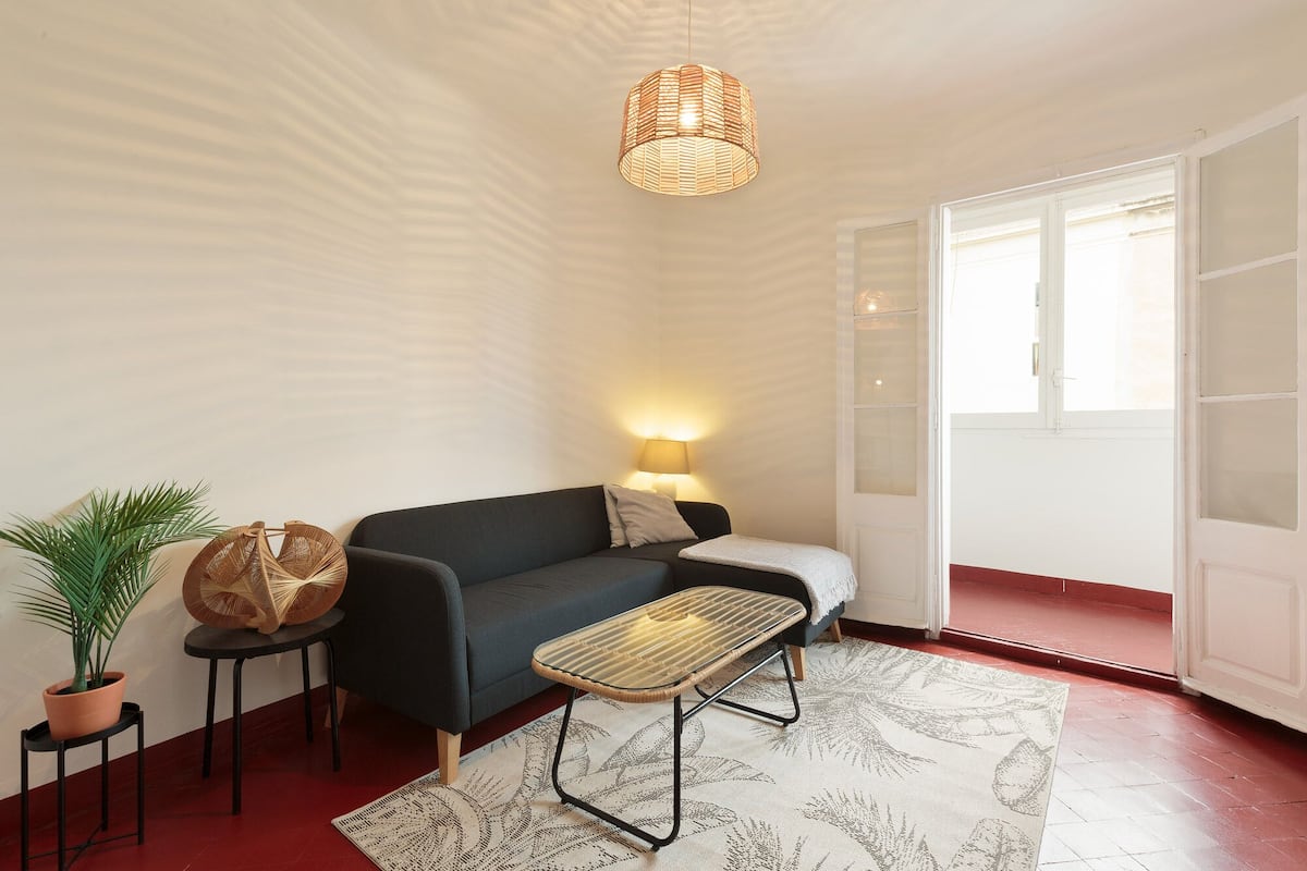 A modern living room with a dark sofa, a small side table, a floor lamp, a potted plant, and a patterned rug.