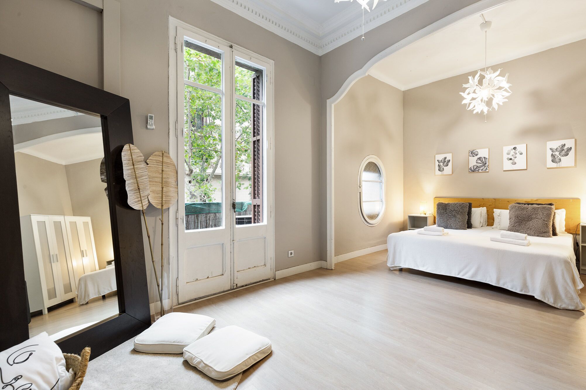 A bedroom with a large bed, a mirror, a window, and artwork on the wall.