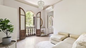 Een ruime woonkamer met een beige bank, een rond tapijt en een potplant.