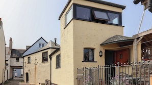 Ein zweistöckiges Haus mit flachem Dach, einem sichtbaren Schornstein und einer Haustür mit rotem Türrahmen.
