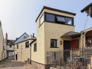 Ein zweistöckiges Haus mit flachem Dach, einem sichtbaren Schornstein und einer Haustür mit rotem Türrahmen.