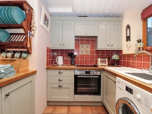 A compact kitchen with a built-in oven, a washing machine, and a sink. - Sammy Hakes Cottage (Watchet)