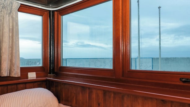 Una stanza con rivestimenti in legno, un letto, ampie finestre e vista sul mare.