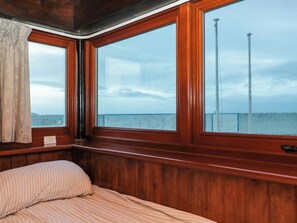 Quarto com painéis de madeira, uma cama, janelas amplas e vista para o mar.
