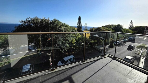 En balkon med frit udsyn til havet og parkerede biler.