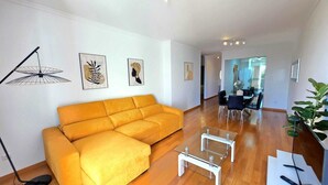 En moderne stue med en gul sofa, et glasbord og kunst på væggene.