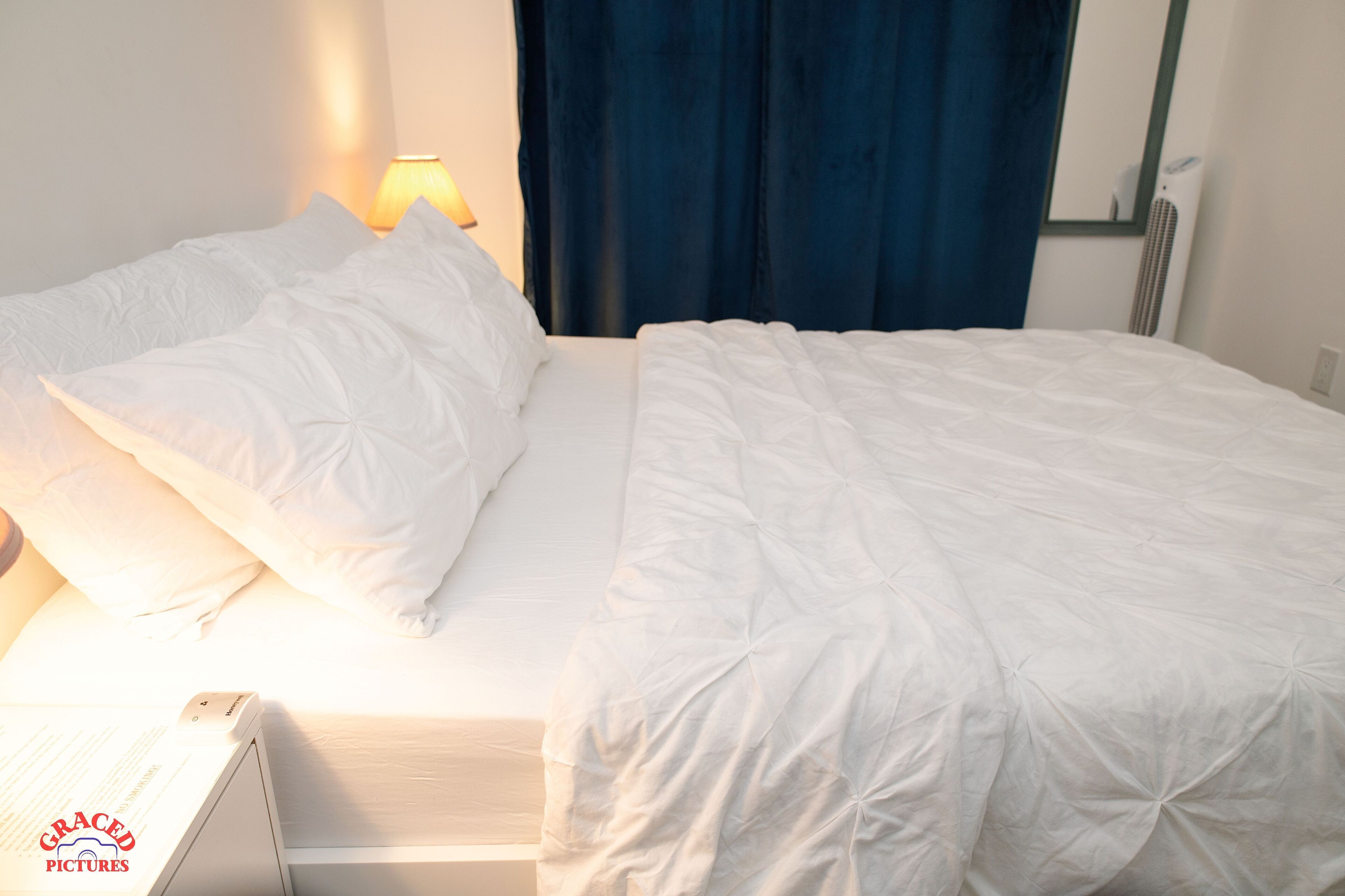 A neatly made bed with white bedding and a lamp on the side.