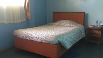 A single bed with a patterned bedspread, a wooden headboard, and a nightstand with a lamp and a book.