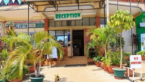 A hotel reception with a sign indicating 'Reception' above the entrance. There are potted plants in front of the hotel, and a 'No Hawking' sign is visible to the right. - Legacy Star Hotel Chuka (Chuka)