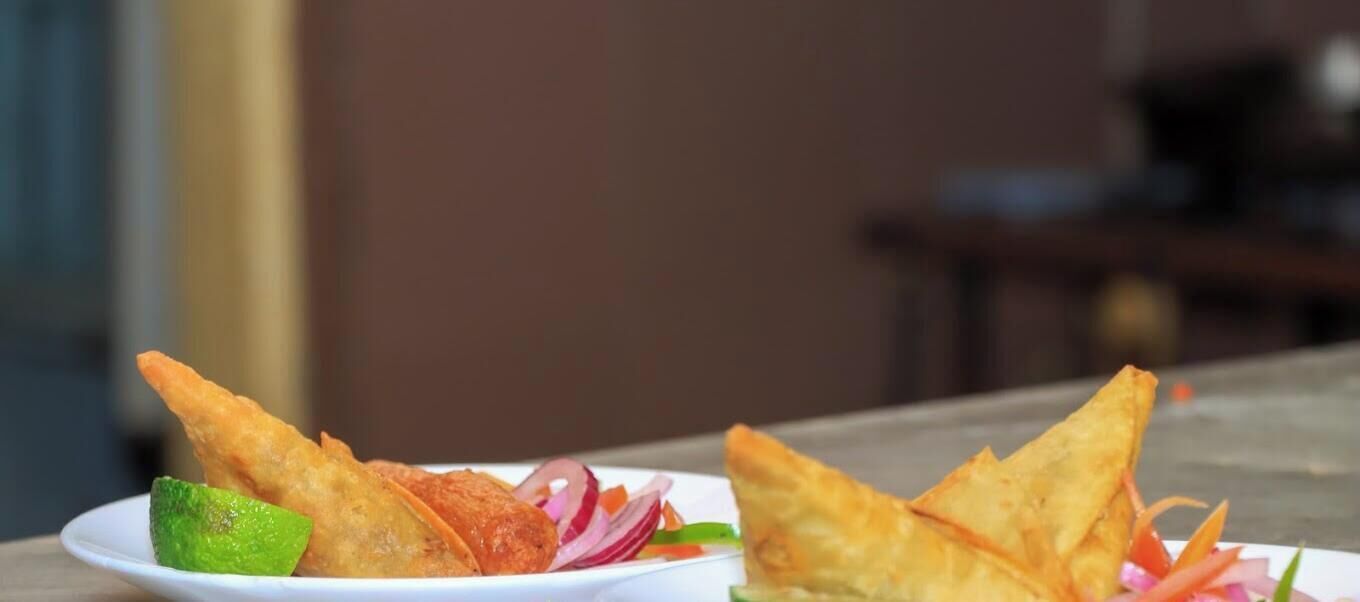Two plates of fried food with lime and sliced vegetables.