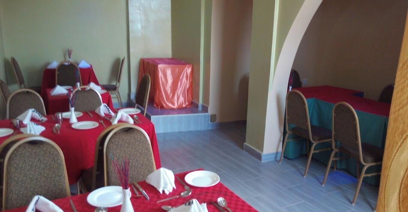Un comedor con mesas dispuestas para una comida, sillas y un pequeño escenario con una mesa cubierta con un mantel rojo.
