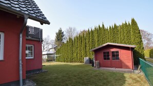 Un bâtiment rouge doté d’un balcon, d’un petit abri de jardin et d’une pelouse bien entretenue.