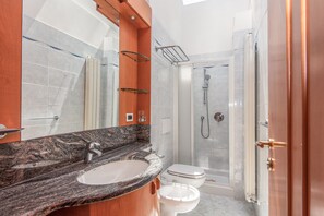A modern bathroom with a granite countertop sink, a mirror, a glass shower enclosure, and a white toilet. - Hotel with private beach in San Vincenzo (San Vincenzo)